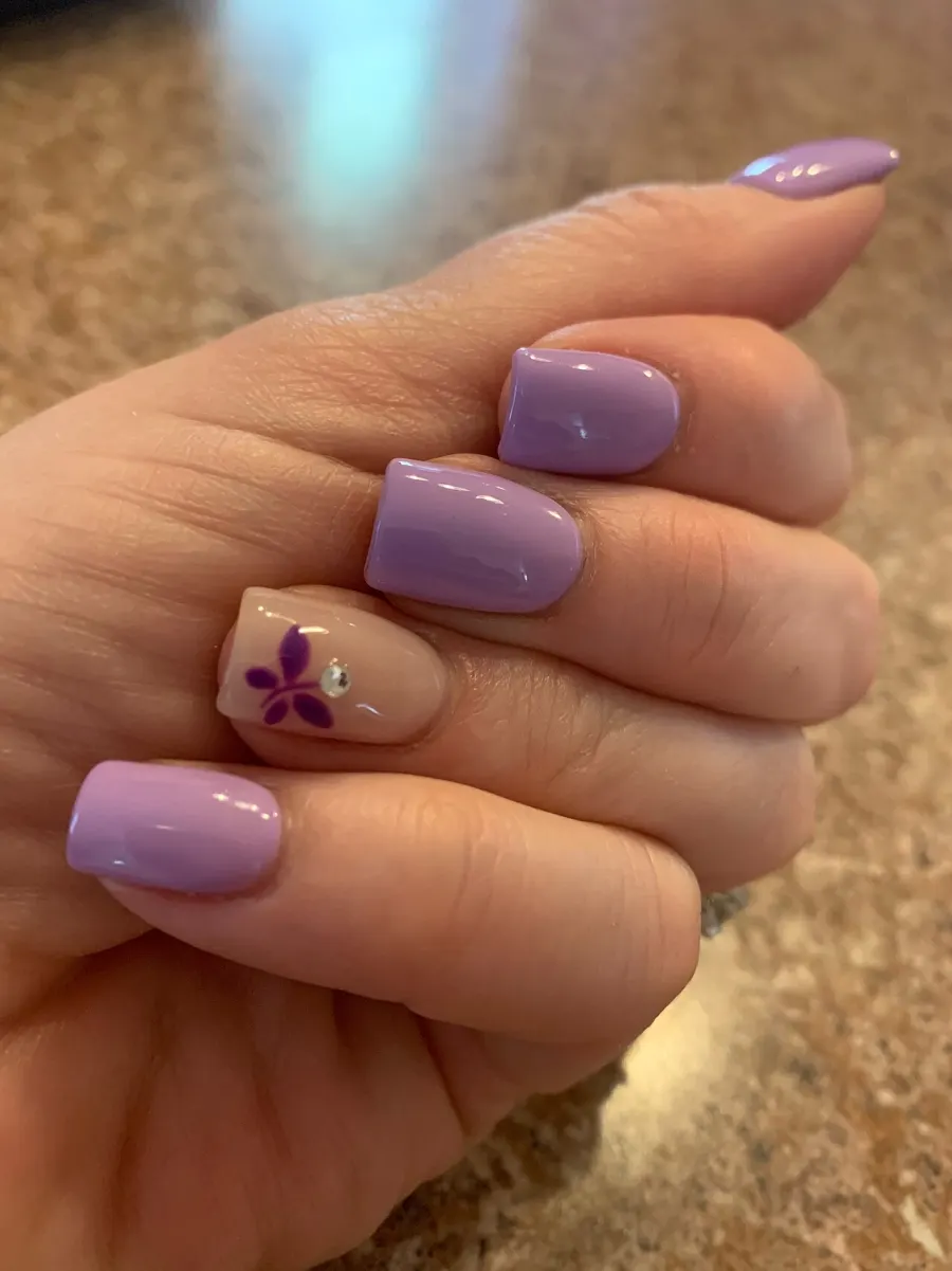 Ongles lilas avec une fleur sur l'annulaire